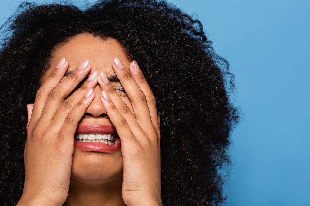 rozrušený africký americký žena obskuring tvář s rukama, zatímco pláč izolovaný na modré - Fotografie, Obrázek