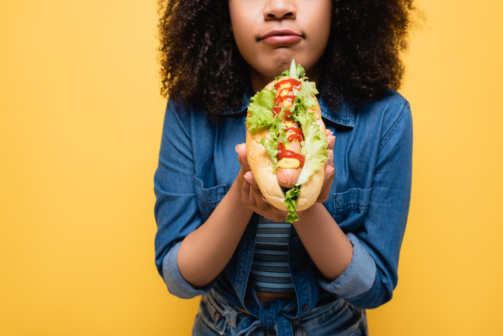 levágott kilátás afro-amerikai nő gazdaság ízletes hot dog elszigetelt sárga - Fotó, kép