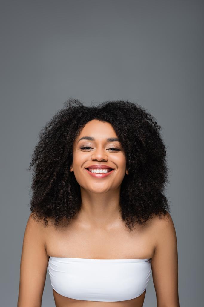 χαρούμενη Αφροαμερικανή γυναίκα με τέλειο δέρμα χαμογελώντας στην κάμερα απομονωμένη στο γκρι - Φωτογραφία, εικόνα