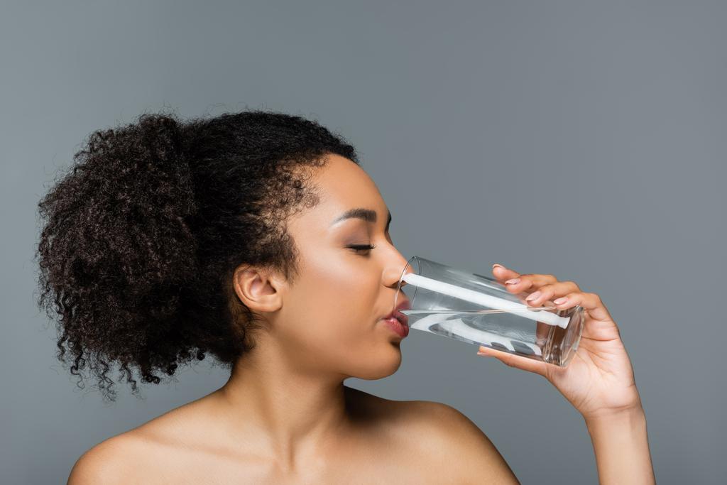 きれいな肌と裸の肩を持つアフリカ系アメリカ人女性が灰色で隔離された飲料水を - 写真・画像