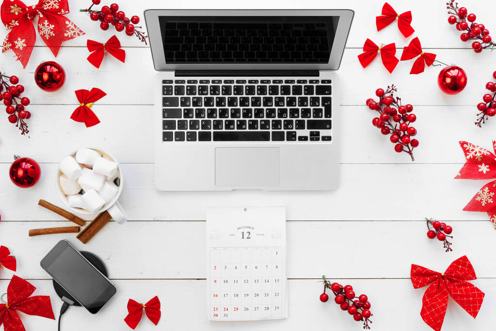 赤いクリスマスの装飾に囲まれた白い木製の机の上のラップトップ、トップビュー - 写真・画像