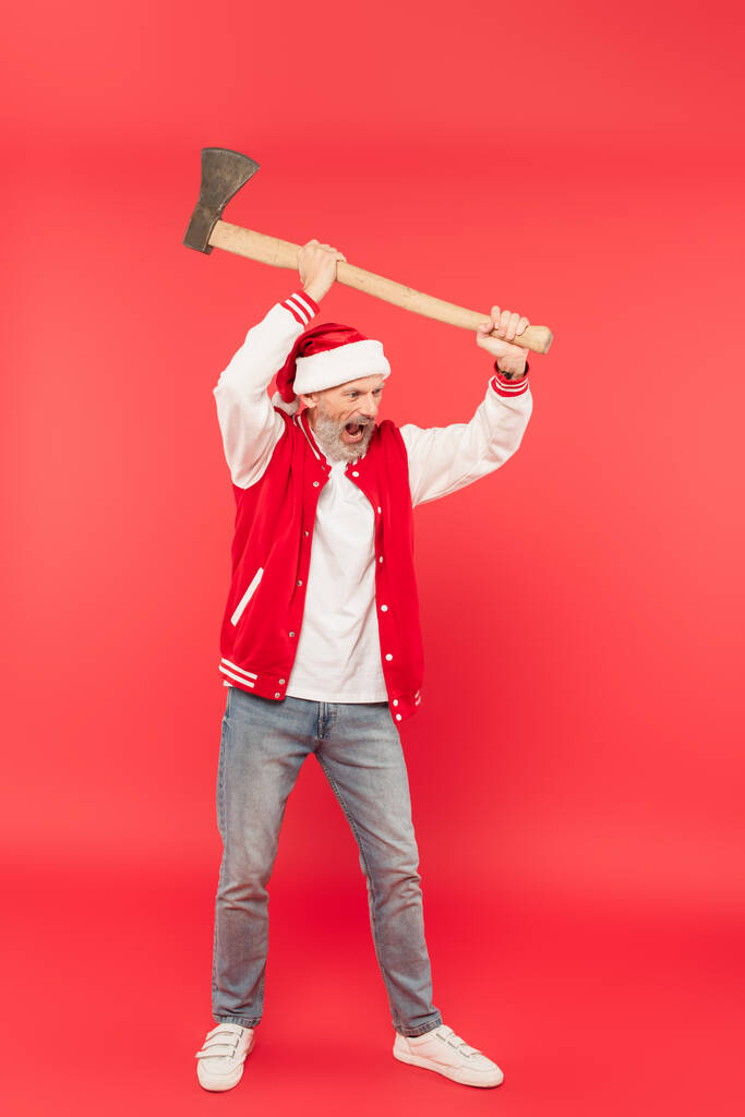 comprimento total do homem de meia idade em santa chapéu segurando machado acima da cabeça e gritando em vermelho - Foto, Imagem