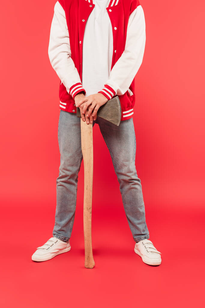 καλλιεργημένη άποψη του ανθρώπου κρατώντας τσεκούρι, ενώ στέκεται στο κόκκινο - Φωτογραφία, εικόνα