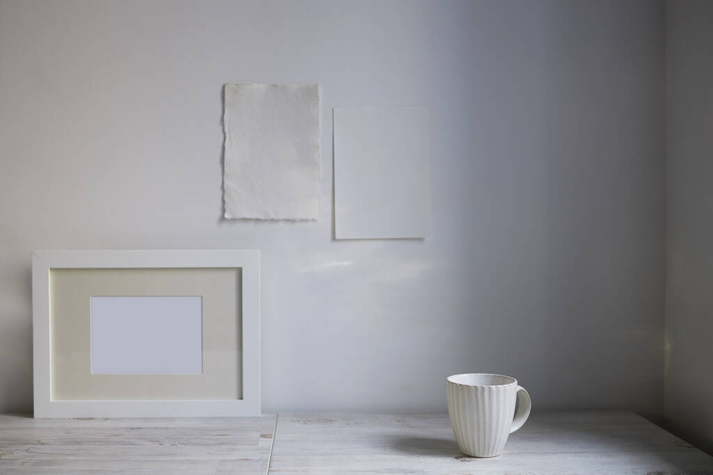 Scandinavian style. Interior Design. A white cup, , a frame for a photo are on the table. Two blank sheets of paper are attached to the wall. Empty space for text - Photo, Image