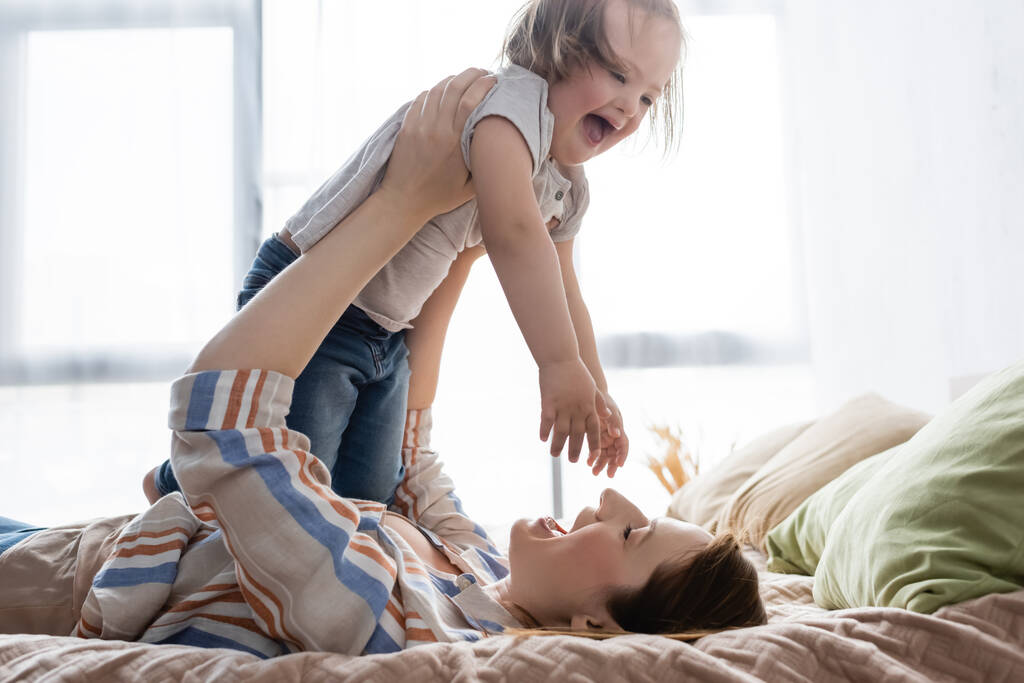 Boldog nő gazdaság izgatott lánya down szindróma az ágyban  - Fotó, kép