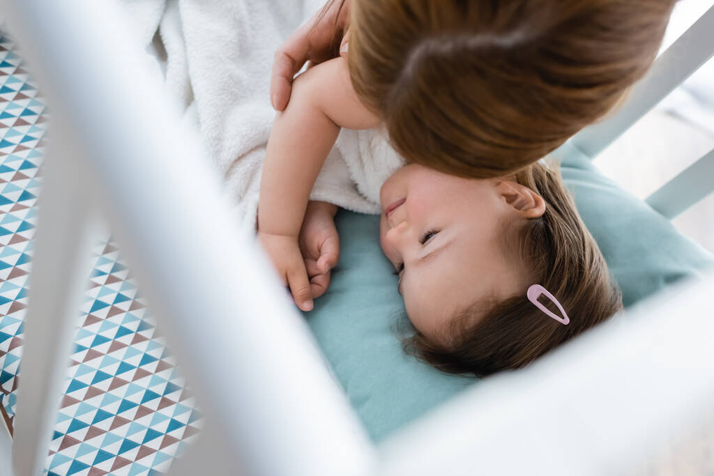 Зовнішній вигляд мами, яка торкається дитини з синдромом Дауна в ліжечку вдома
  - Фото, зображення