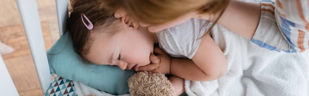 Bovenaanzicht van moeder aanraken slapende dochter met down syndroom in baby wieg, banner  - Foto, afbeelding