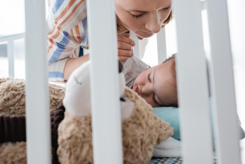 Η μητέρα κοιτάζει το μωρό που κοιμάται με σύνδρομο Down στην κούνια του μωρού  - Φωτογραφία, εικόνα