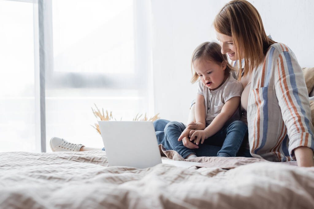 Glückliche Eltern zeigen auf Laptop neben Tochter mit Down-Syndrom im Bett  - Foto, Bild