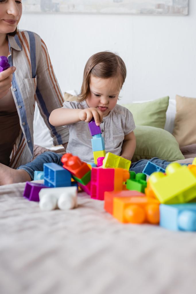 Girl with down syndrome playing building blocks on bed near mother  - Photo, Image