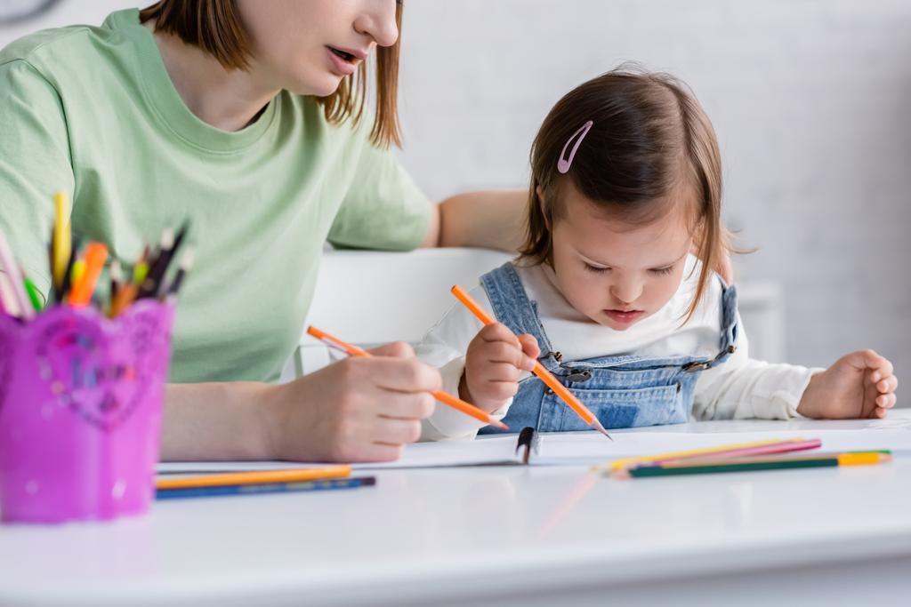 Genitore seduto vicino a figlia con sindrome di Down disegno su carta a casa  - Foto, immagini