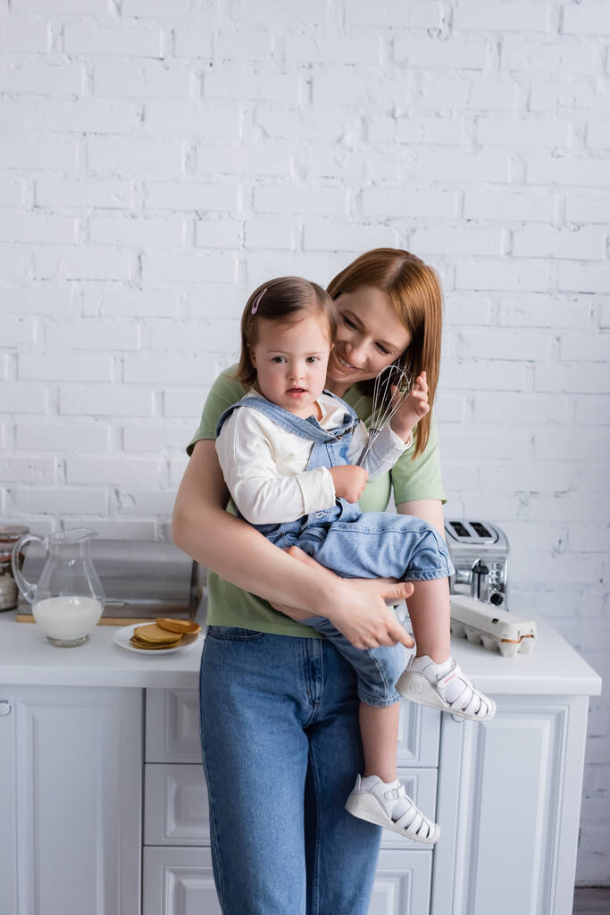 Счастливая мать держит дочь с синдромом Дауна и вскочить на кухню  - Фото, изображение