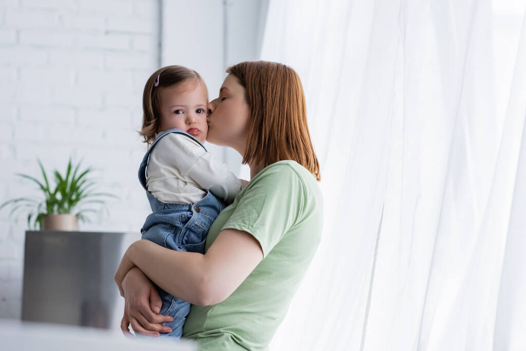 Мать целует ребенка с синдромом Дауна на кухне  - Фото, изображение