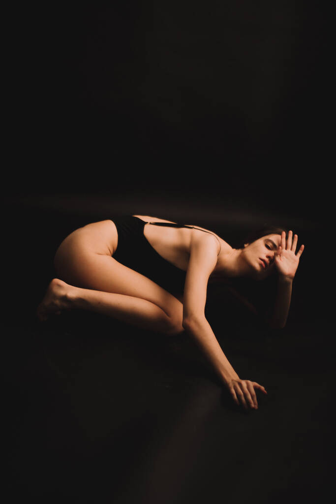 uma menina morena em um bodysuit sincero expressa livremente emoções e danças na câmera. sessão de fotos em um fundo preto - Foto, Imagem