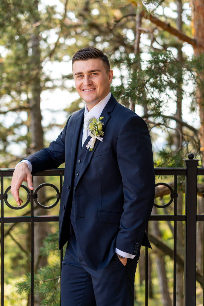 Knappe jonge bruidegom draagt een elegant en stijlvol donkerblauw outdoorportret. Gelukkig bruidegom kijken en glimlachen op de camera. - Foto, afbeelding