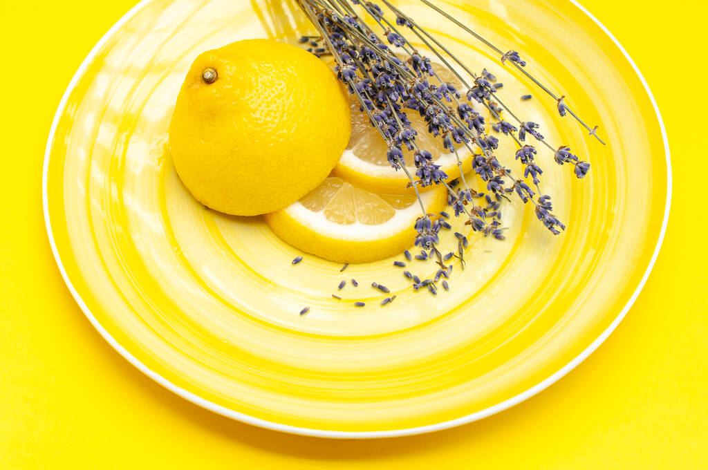 Keltainen mehukas sitruuna ja laventeli yrtti keltaisella levyllä viipaloitu kauniisti. Hedelmät tarjoillaan käsite  - Valokuva, kuva