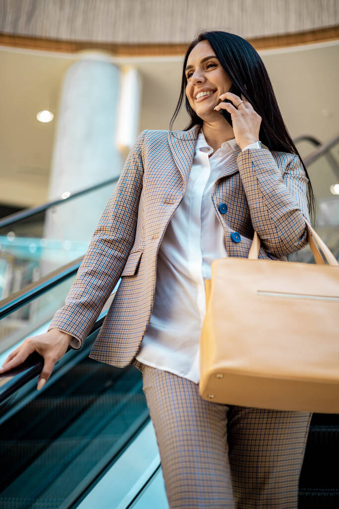Smiling business woman buyer posing at escalator and talking smartphone - Photo, Image
