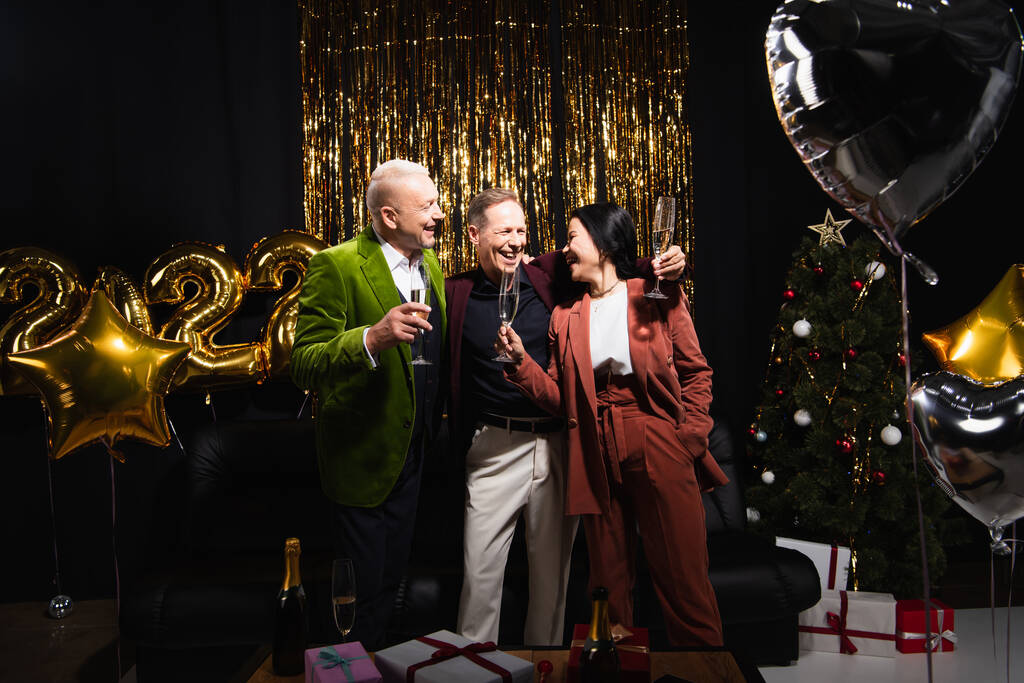 Pozitív többnemzetiségű barátok pezsgővel közel léggömbök és karácsonyfa fekete háttér  - Fotó, kép