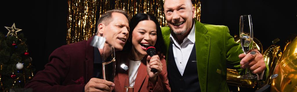 Asiatin singt Karaoke bei Freunden mit Champagner bei Neujahrsparty auf schwarzem Hintergrund, Banner  - Foto, Bild