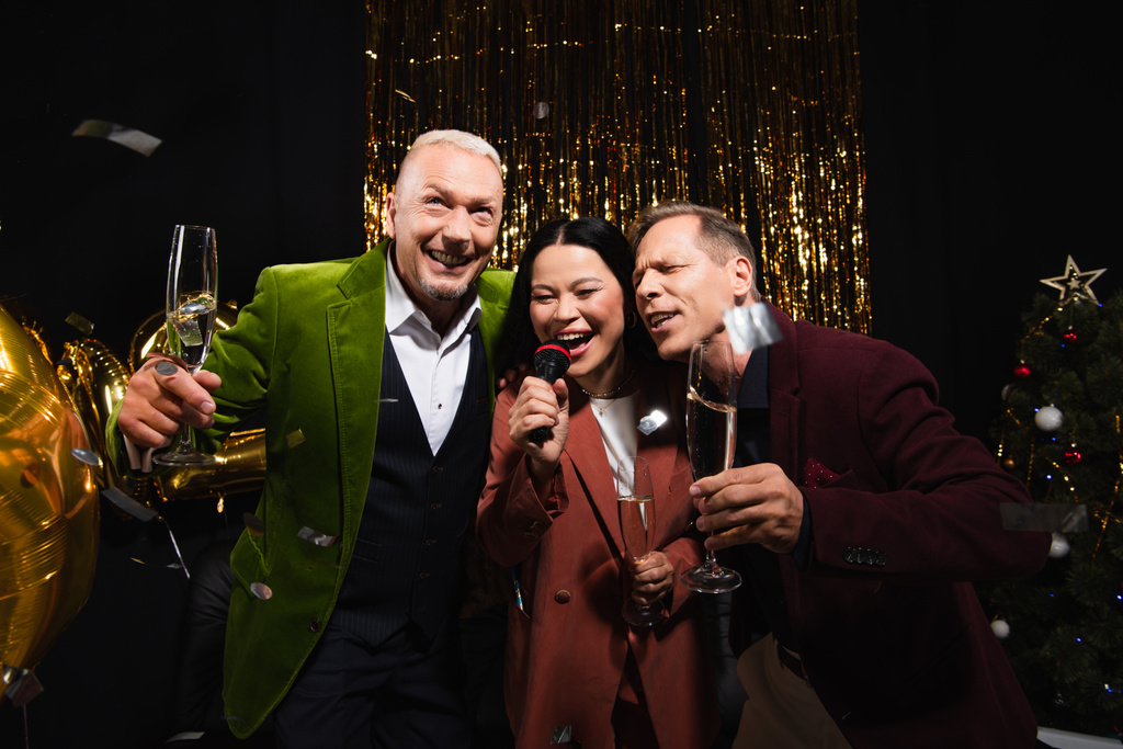 Boldog érett fajok közötti barátok pezsgővel éneklő karaoke újévi party fekete alapon  - Fotó, kép