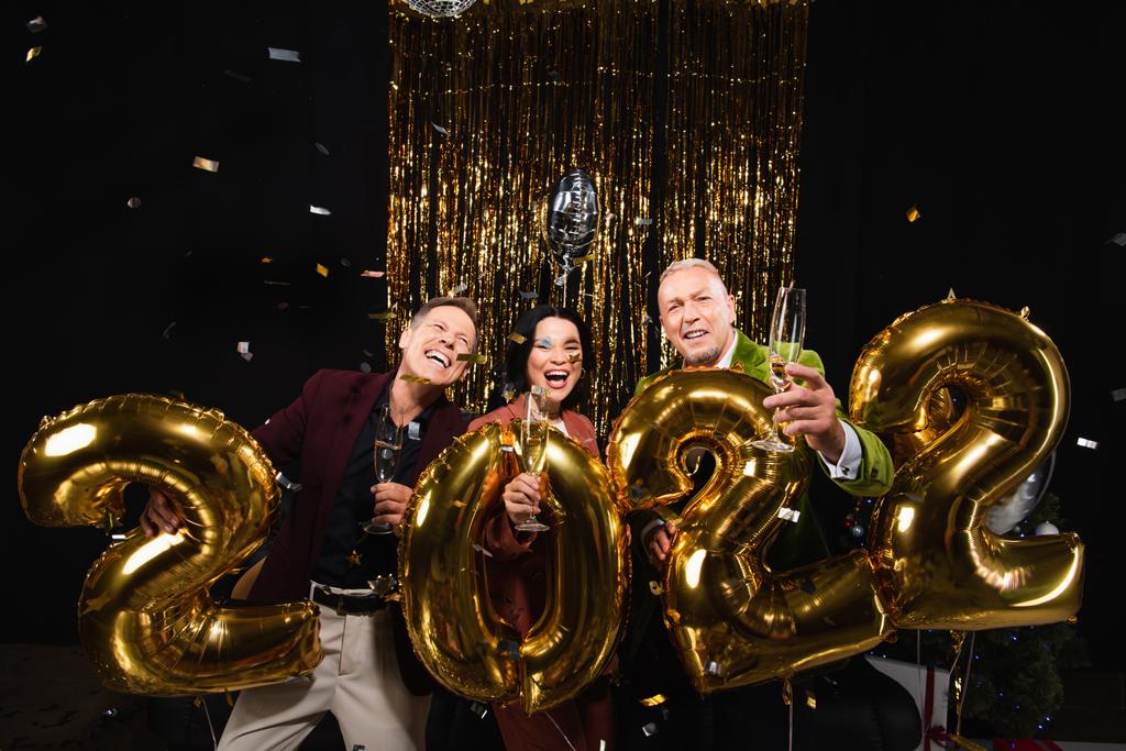 Щасливі багатоетнічні зрілі друзі тримають шампанське біля кульок у формі 2022 року на чорному тлі
  - Фото, зображення