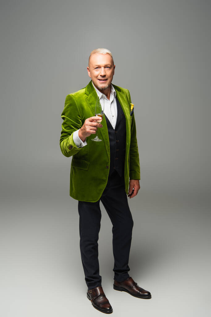 Hombre positivo en ropa formal sosteniendo copa de champán sobre fondo gris  - Foto, Imagen