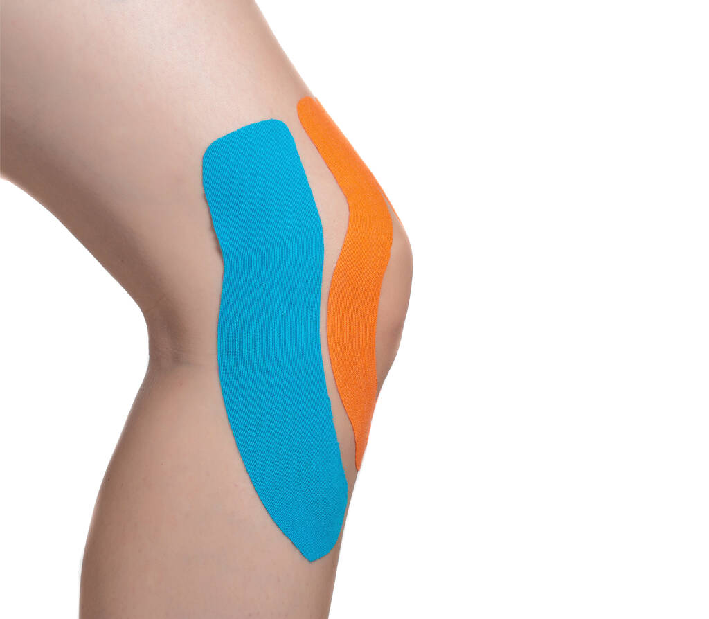 Articulação do joelho feminino com fita laranja e azul para microcirculação e fixação articular. Fundo branco, isolar - Foto, Imagem