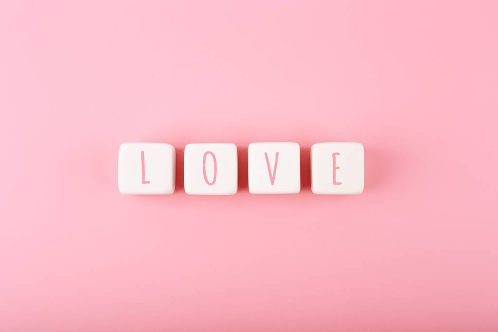 Слово любовь написана на белых кубиках игрушки на розовом фоне с копировальным пространством. Минимальная модная концепция Дня Святого Валентина, любовных эмоций, юбилеев или свиданий - Фото, изображение