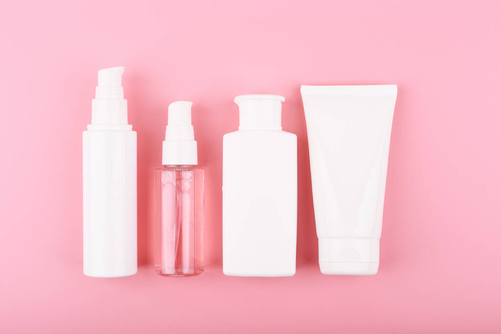 Moderna y moderna cama plana minimalista con un conjunto de productos de belleza en tubos blancos en fila sobre fondo rosa. Concepto de rutina diaria de cuidado de la piel  - Foto, imagen