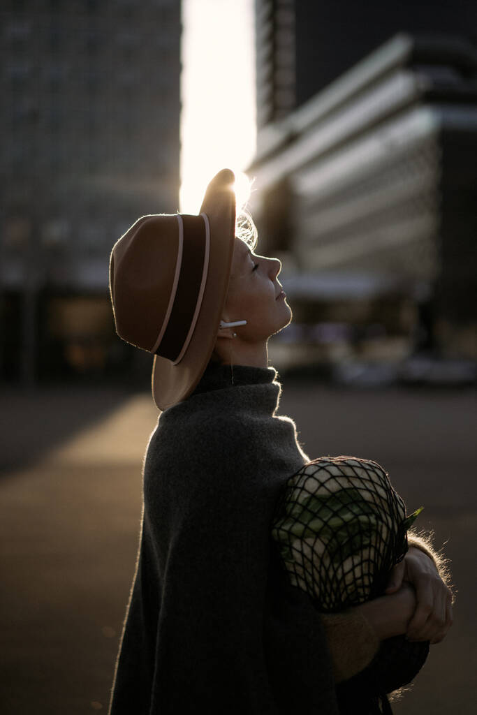 Hermosa mujer de mediana edad en un sombrero con un corte de pelo corto en el centro de una gran ciudad. Retrato de primer plano, luz de fondo suave. - Foto, imagen