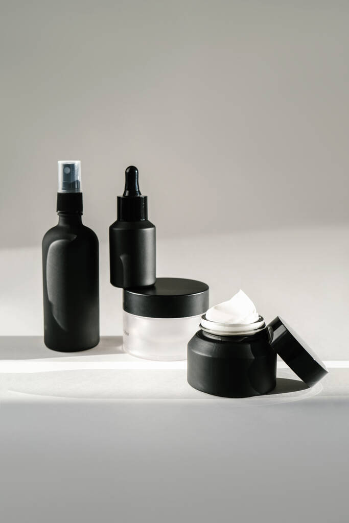 Vier schwarze Kosmetikflaschen auf einem sonnendurchfluteten Hintergrund. - Foto, Bild