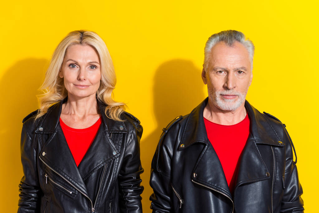 Porträt von zwei attraktiven, zufriedenen grauhaarigen Ehepartnern, die einen coolen Look auf leuchtend gelbem Hintergrund tragen - Foto, Bild
