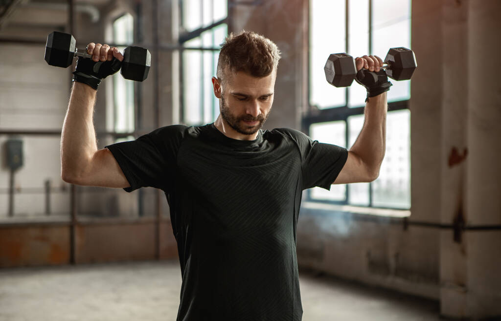 Strong man exercising with dumbbells in gym - Photo, Image
