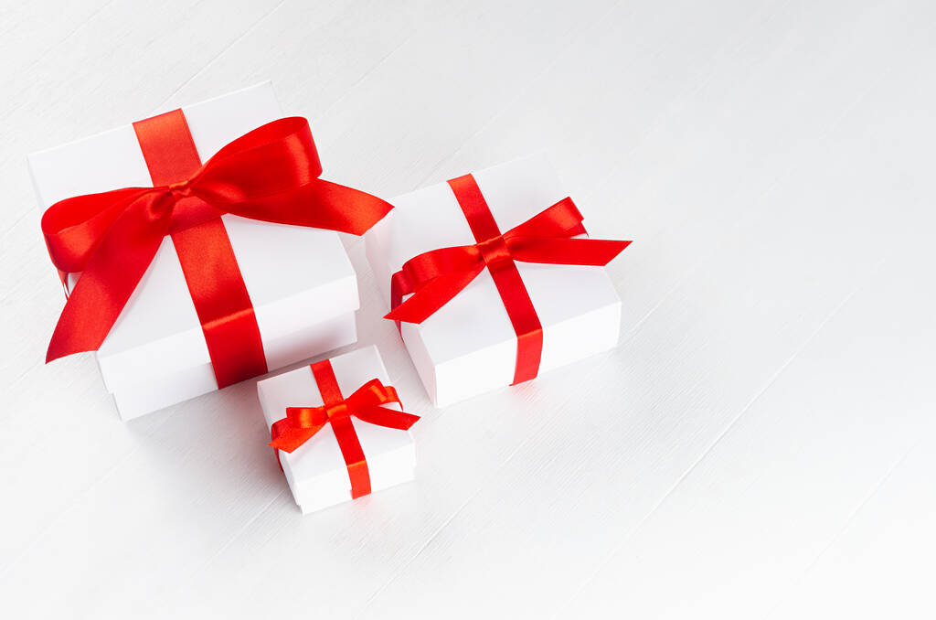 Boîtes cadeaux blanches de différentes tailles avec ruban de satin rouge et arc sur table blanche vue dessus, espace de copie. Fond festif pour la conception de la carte, brochure, couverture, dépliant. - Photo, image