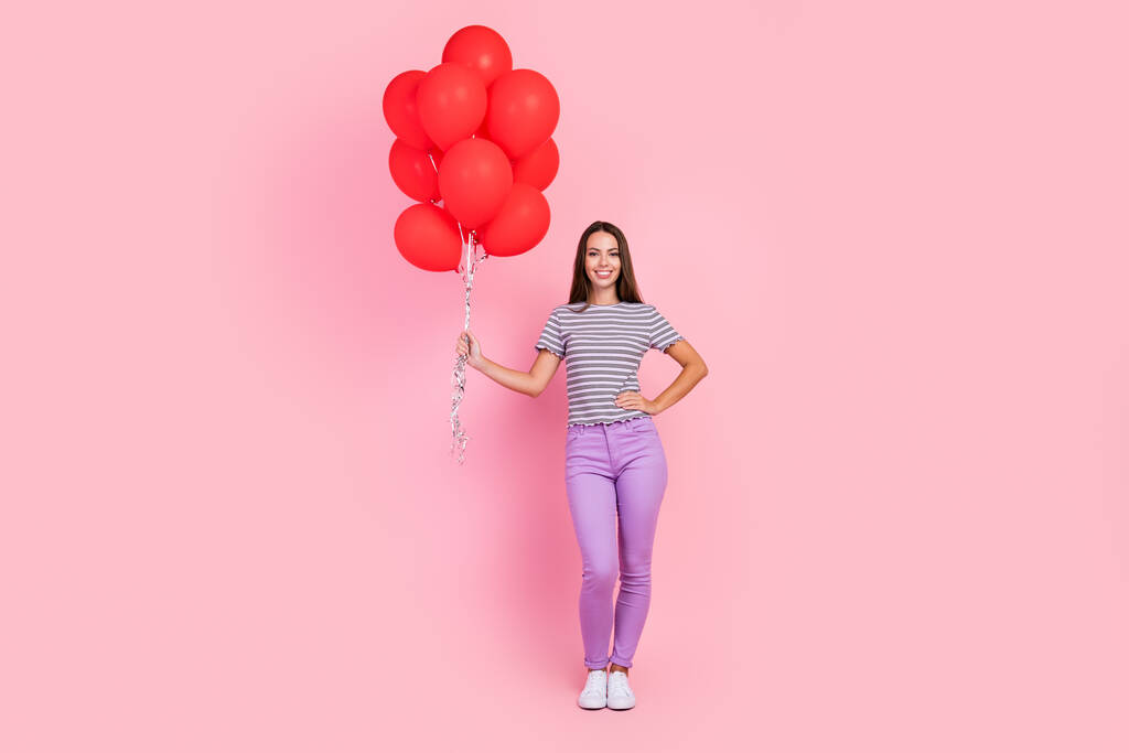 Фото красивої молодої леді в смугастому вбранні, посміхаючись, тримає букет повітряних кульок ізольований рожевий колір фону
 - Фото, зображення