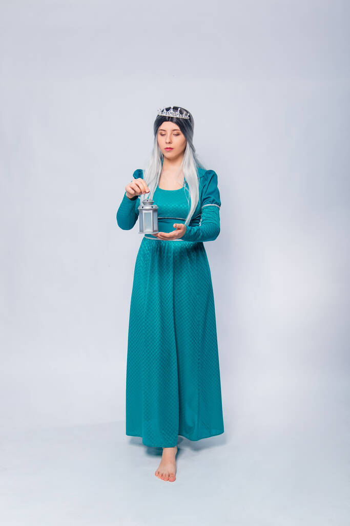 Полный портрет принцессы в средневековом, фантазийном, бирюзовом платье с ясенем и серебряной короной, позирующей с лампой в руках, изолированной на белом фоне. - Фото, изображение