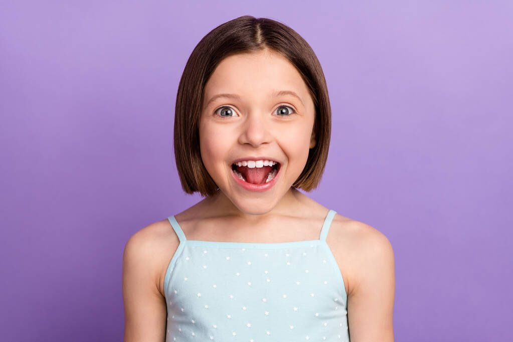 Zdjęcie śmieszne brązowe włosy mała dziewczyna otwarte usta nosić niebieski top izolowane na fioletowym tle koloru - Zdjęcie, obraz
