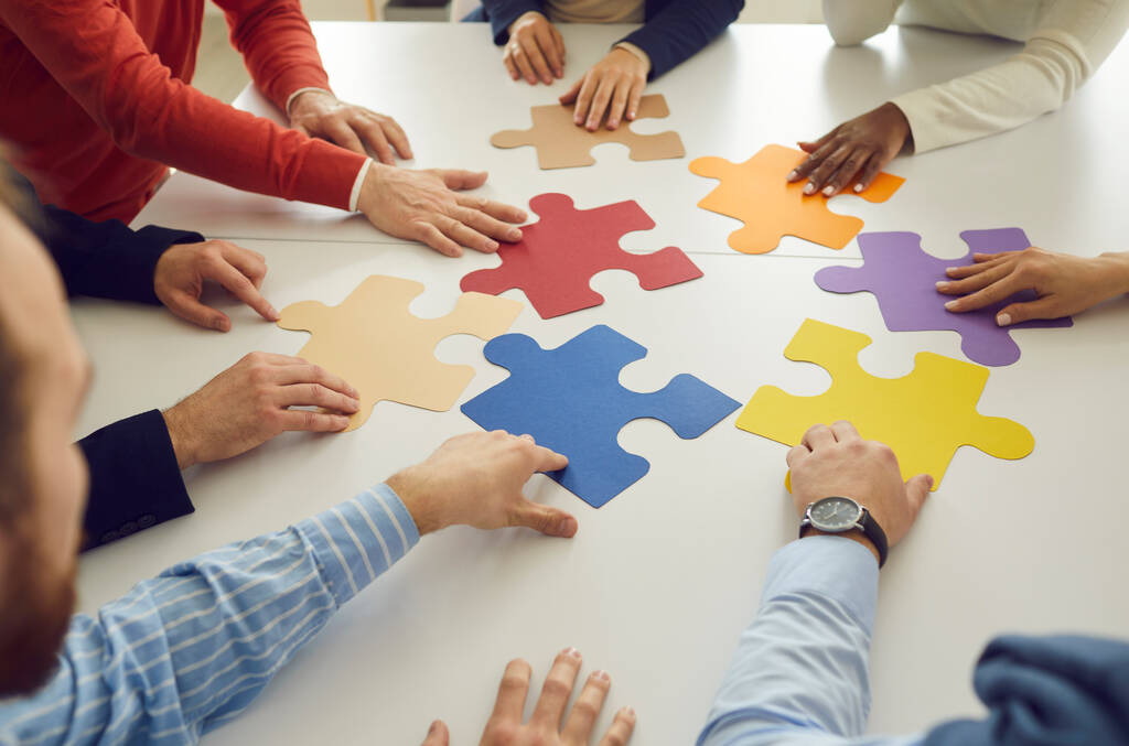Multiraciale zakenlieden die in een cirkel aan een tafel zitten en stukjes van een gekleurde puzzel vormen. - Foto, afbeelding