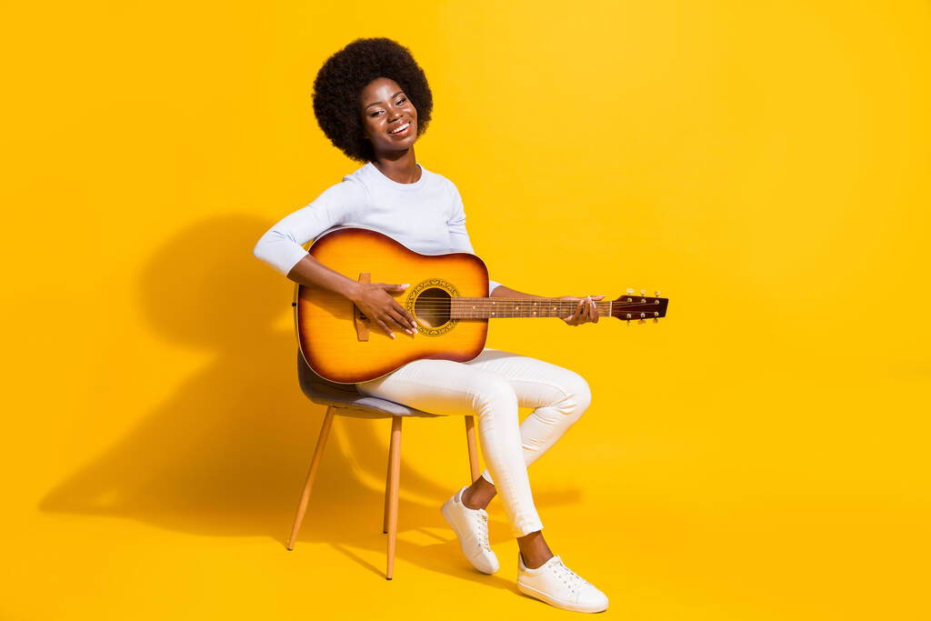 Retrato de perfil de longitud completa de adorable chica de piel oscura alegre tocando la guitarra aislada sobre fondo de color amarillo - Foto, imagen