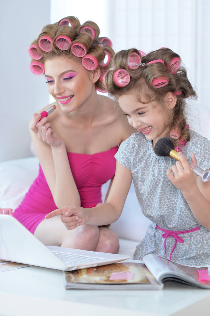  madre e hija con rizadores de pelo que se aplican maquillaje  - Foto, imagen