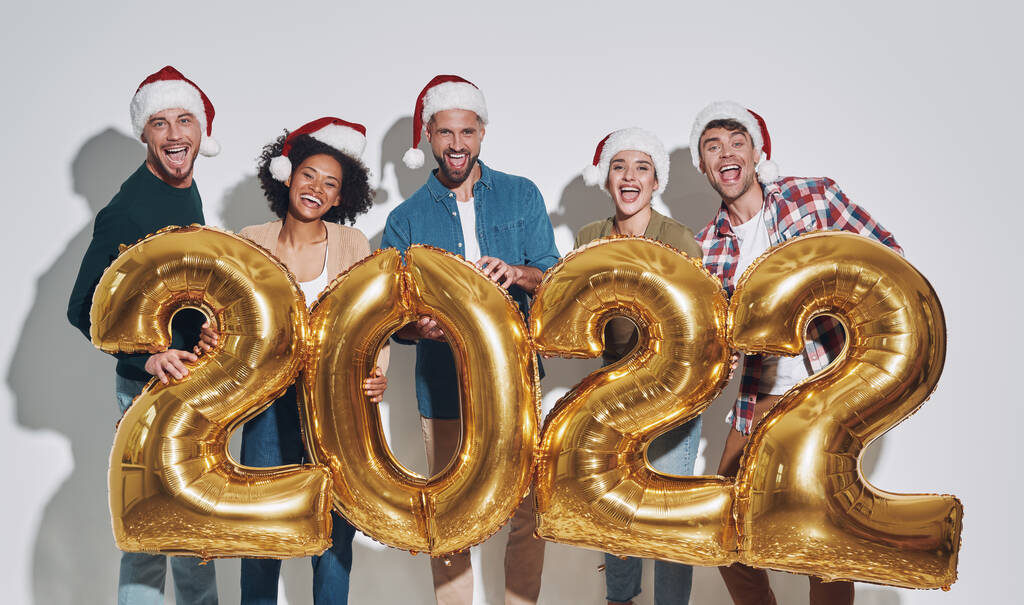 Altın renkli numaralar taşıyan ve gülümseyen Noel şapkalı bir grup güzel insan. - Fotoğraf, Görsel
