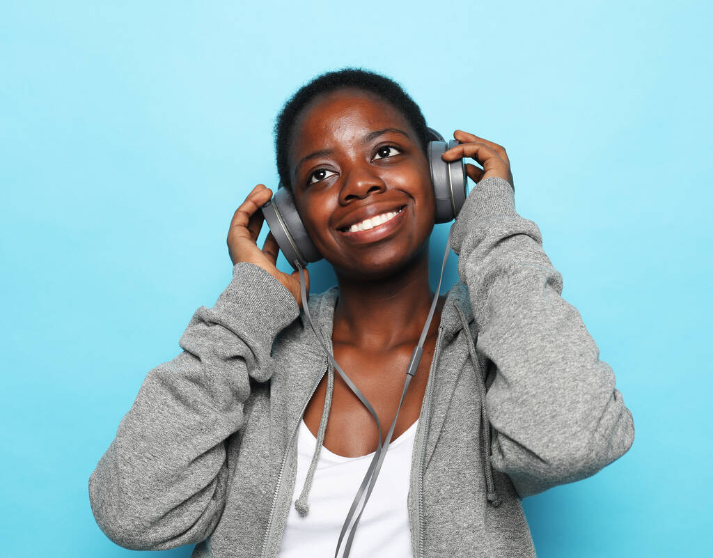 Belle jeune femme afro-américaine écouter de la musique sur fond bleu. - Photo, image