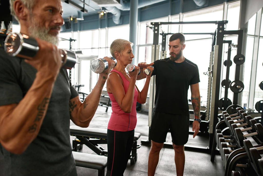 Determined senior woman and man with dumbbells in gym - Photo, Image