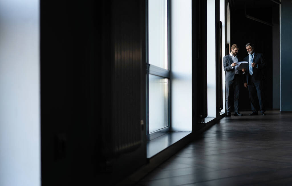Dwóch kolegów komunikujących się w korytarzu, partnerzy spacerujący w nowoczesnym biurze - Zdjęcie, obraz
