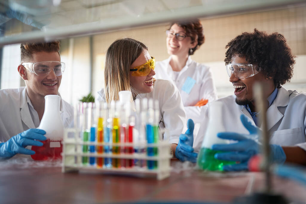 Jonge scheikundestudenten die zich vermaken in een steriele laboratoriumomgeving terwijl ze werken met kleurrijke chemicaliën. Wetenschap, scheikunde, lab, mensen - Foto, afbeelding