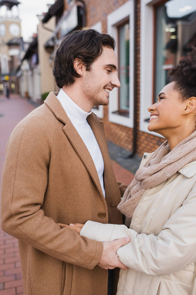 boční pohled šťastný muž s úsměvem při objímání africké americké přítelkyně venku - Fotografie, Obrázek