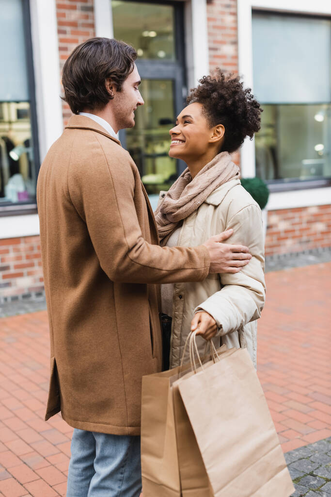 mulher americana africana alegre segurando sacos de compras e olhando para o namorado ao ar livre  - Foto, Imagem