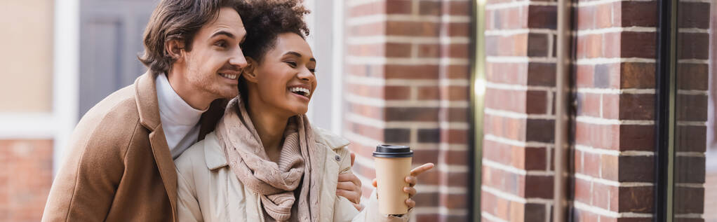heureuse femme afro-américaine avec tasse en papier pointant vers le bâtiment près du petit ami, bannière - Photo, image