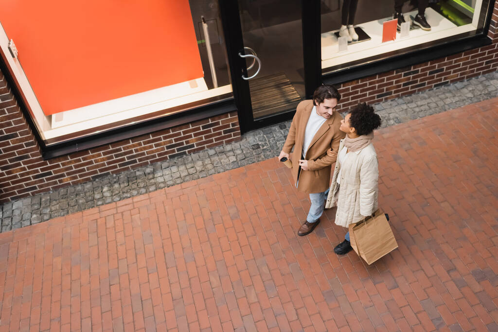 высокий угол обзора радостной межрасовой пары с покупками ходить в торговом центре  - Фото, изображение