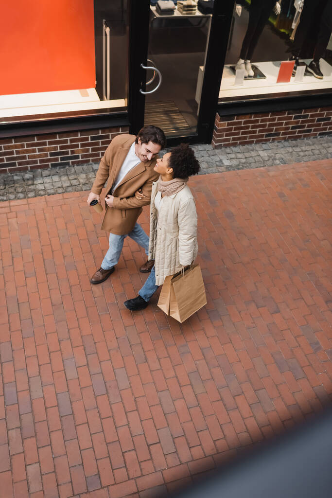 vista de ángulo alto de alegre pareja multiétnica con compras caminando en el centro comercial  - Foto, imagen